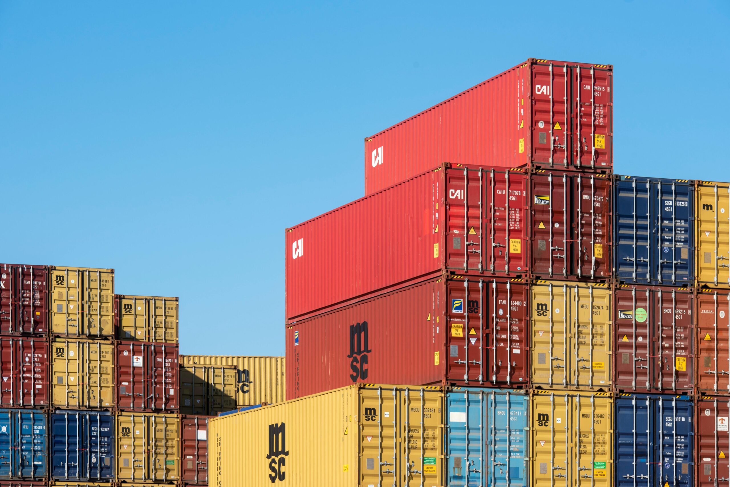 A vibrant collection of stacked shipping containers under a clear, blue sky. Ideal for logistic themes.